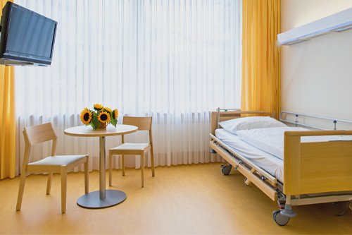 Койка и стол со стульями в палате с жёлтыми занавесками